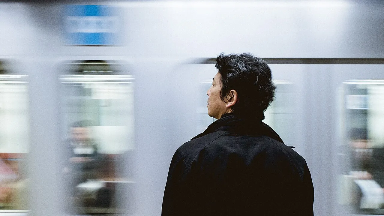 Hombre esperando en un andén mientras pasa un tren
