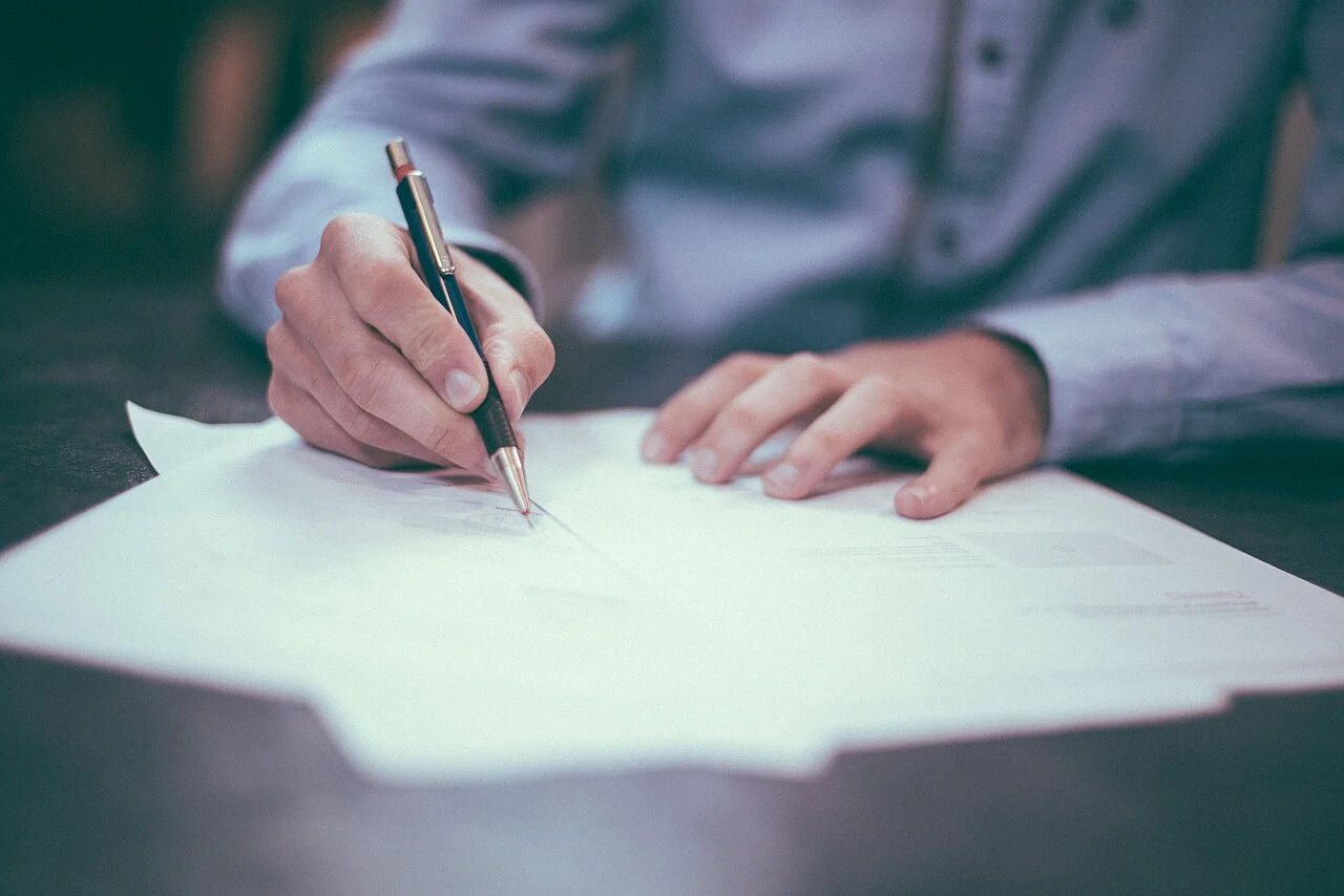 Persona firmando unos documentos con bolígrafo sobre una mesa